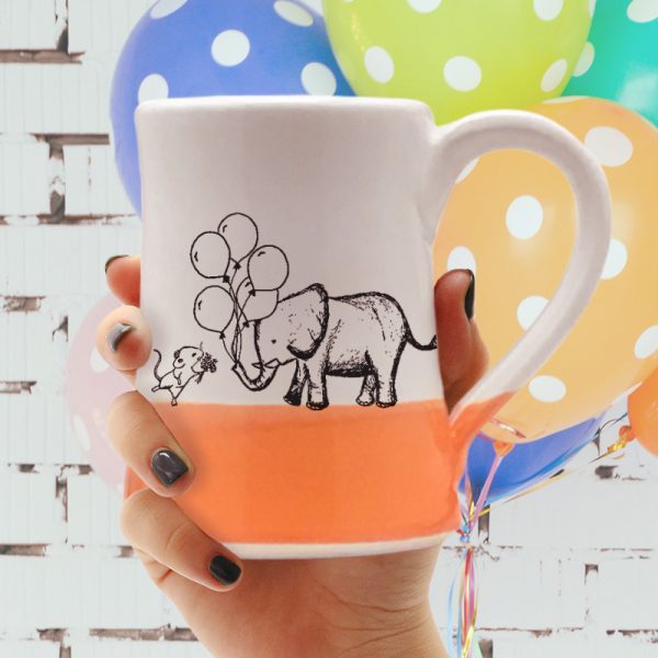Handmade coffee mug with a drawing of a mouse and an elephant bringing each other gifts. Coral accent color.