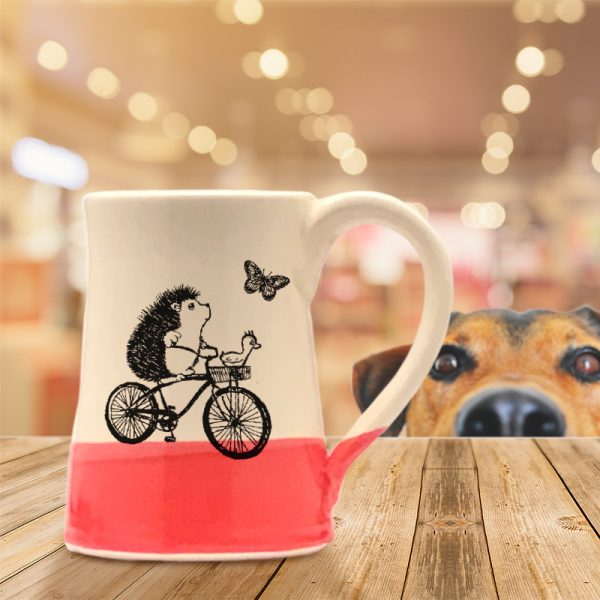 Handmade coffee mug with drawing of a hedgehog riding a bicycle while the duck navigates. Red accent color.