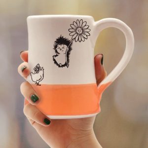 Coffee mug with drawing of a hedgehog flying on a flower to meet a surprised chicken. Coral accent color. Handmade in the USA by crafty hedgehogs.