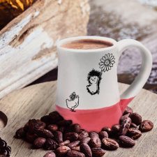 Coffee mug with drawing of a hedgehog flying on a flower to meet a surprised chicken. Red accent color. Handmade in the USA by crafty hedgehogs.