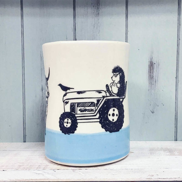 tumbler with drawing of a hedgehog in overalls riding a tractor with a cow in front