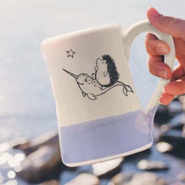 Handmade coffee mug with original illustration of a hedgehog riding on the back of a narwhal. Lavender accent color. Made by little crafty hedgehogs.