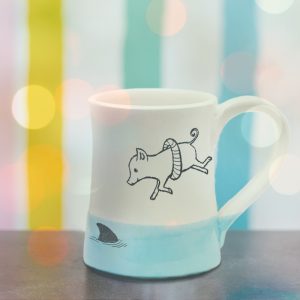 Handmade coffee mug with illustration of a piglet in a life ring bravely diving into shark infested waters. Light blue accent color. Made by hedgehogs in the Blue Ridge Mountains.