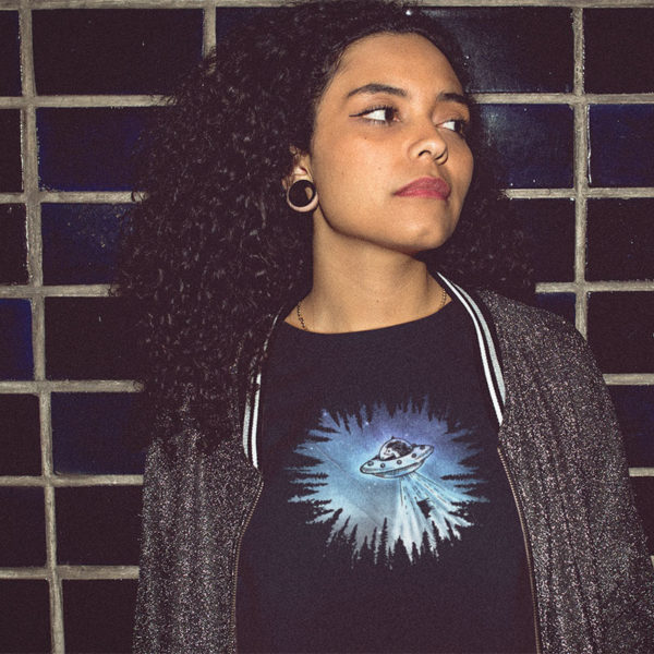 Woman wearing graphic T-shirt with original drawing of a hedgehog piloted UFO stealing a cow