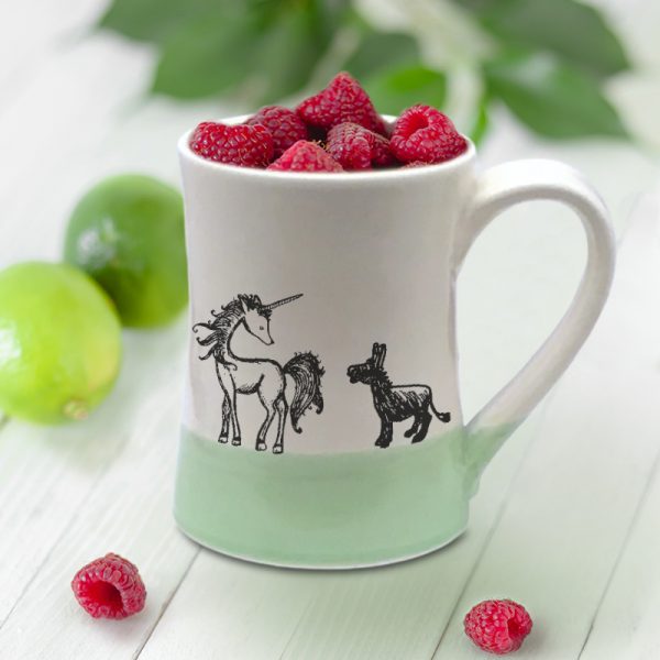 A handmade coffee mug with an illustration of a lovely unicorn and a pathetic little donkey who is in love. Green accent color.