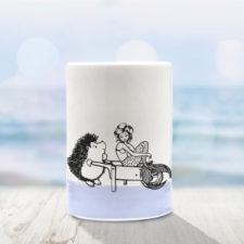 Handmade ceramic tumbler with drawing of a hedgehog and a mermaid in a wheelbarrow. Lavender accent color