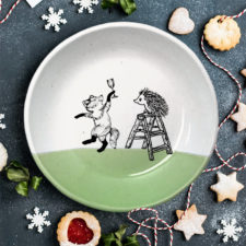This plate is handmade by the hedgehogs of Darn Pottery and has a drawing of a fox celebrating with a champagne and a hedgehog climbing a ladder. Green accent color.