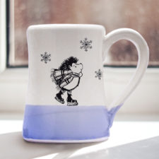 Handmade coffee mug with a drawing of a hedgehog ice skating and looking dapper. Lavender accent color.