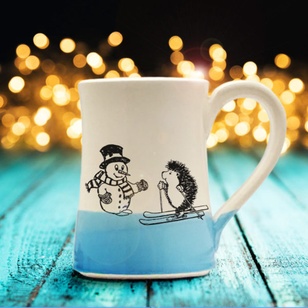 Handmade coffee mug with a drawing of a hedgehog on skis greeting a well-dressed snowman. Blue accent color