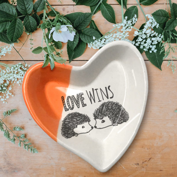 Handmade ceramic heart-shaped dish with drawing of two hedgehogs and the words Love Wins. Coral accent color