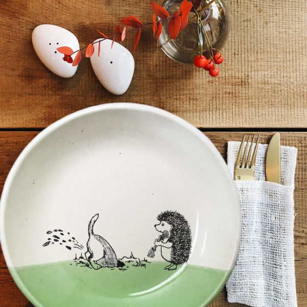 This ceramic plate is handmade by hedgehogs at Darn Pottery and has a drawing oof a dog digging in the yard while hedgehog looks on. Green accent color