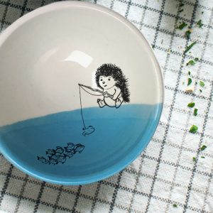 This soup bowl is for the fisherman or woman in your life. It holds fish stew, cereal or minestrone with equal panache and features a drawing of a hedgehog fishing. Blue accent color.