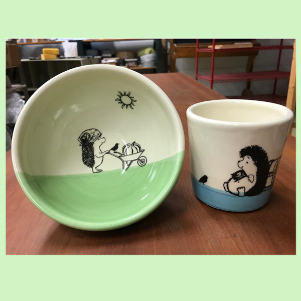 handmade ceramic soup bowl with drawing of a hedgehog gardener and a small cup with a drawing of a hedgehog treasure hunter.