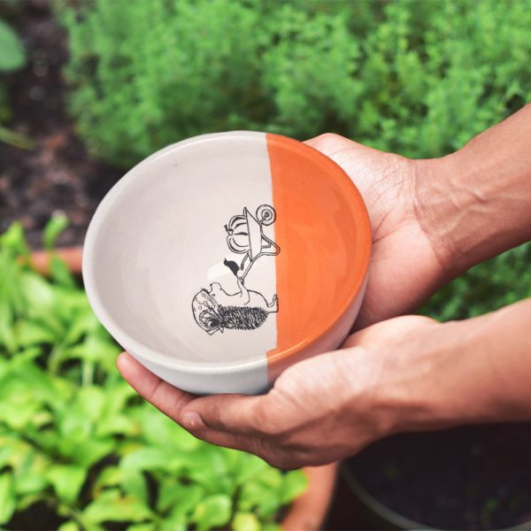 A happy little hedgehog is rolling a wheelbarrow with a giant pumpkin. This cute illustration is featured on a lovely handmade ceramic soup or salad bowl from Darn Pottery. Coral accent color