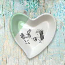Handmade ceramic heart-shaped dish with drawing of a famer hedgehog talking to her chicken. Green accent color