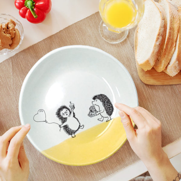 Handmade ceramic salad plate with drawing of hedgehogs wishing each other happy birthday. Gold accent color