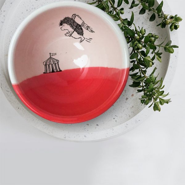 A hedgehog with a jetpack is flying away from the circus.This is happening inside this lovely ceramic soup bowl made by hand in Tennessee. Red accent color