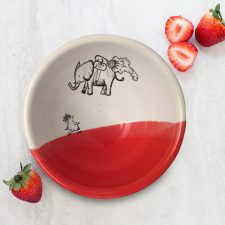 A perfectly sized handmade ceramic bowl for soup with a drawing of an elephant flying over a startled chicken. Red accent color