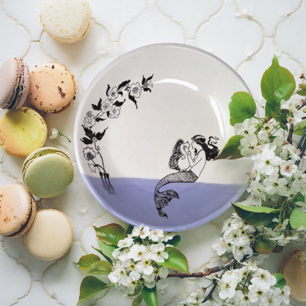 A handmade salad plate with drawing of a mermaid kissing a hedgehog. Lavender accent color