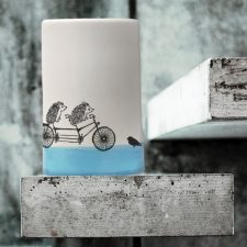 A handmade tumbler with a drawing of two hedgies riding a tandem bicycle. Made by the hedgehogs of Darn Pottery to celebrate the ride. Blue accent color.