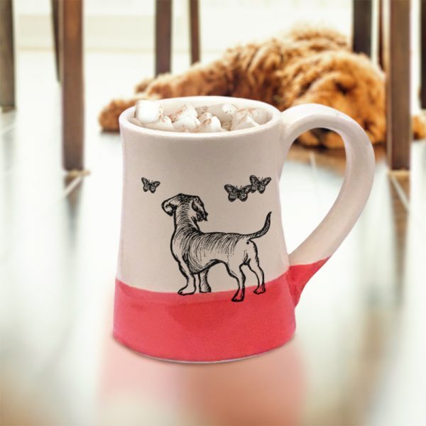 A handmade coffee mug with a drawing of a doggie hanging out with a bunch of butterflies. Red accent color.