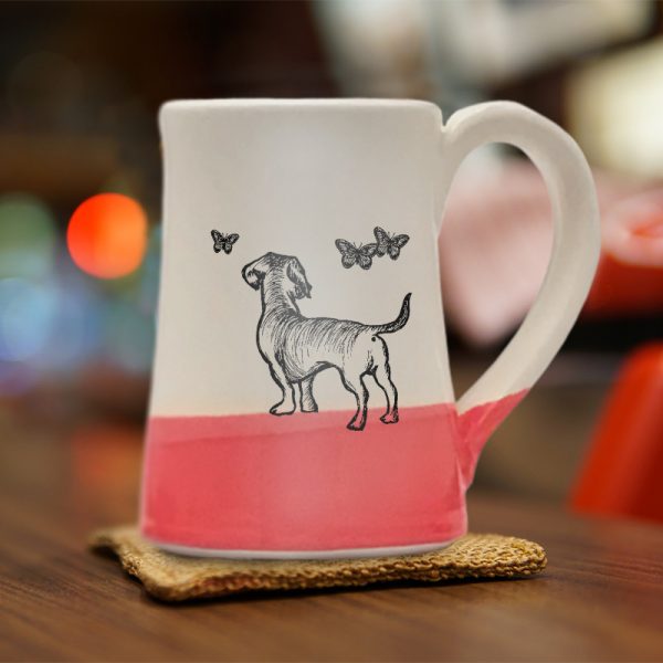 A handmade coffee mug with a drawing of a doggie hanging out with a bunch of butterflies. Red accent color.