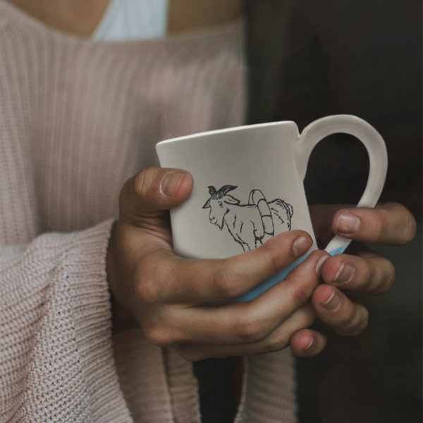 Handmade coffee mug with a drawing of a goat reconsidering his impulsive decision to swim with the sharks. Blue accent color.