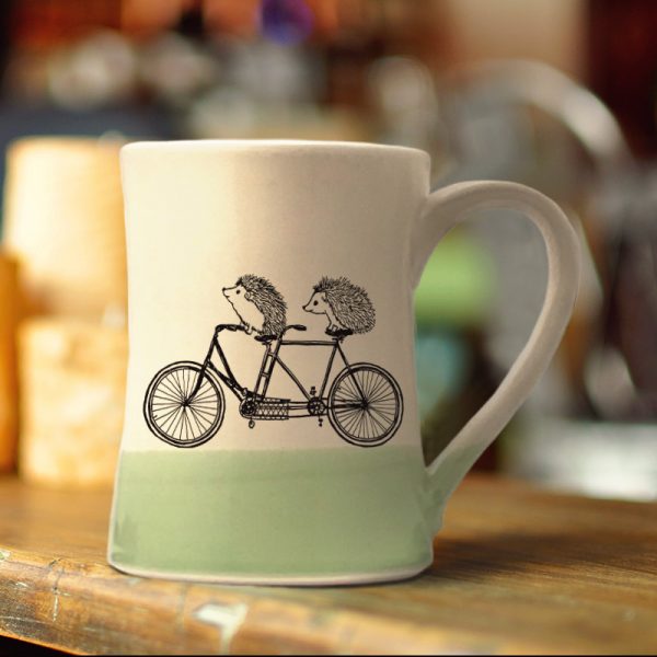 Handmade coffee mug with two happy hedgehogs on a tandem bike. Perhaps they are just married. Or besties out for a ride. Green accent color