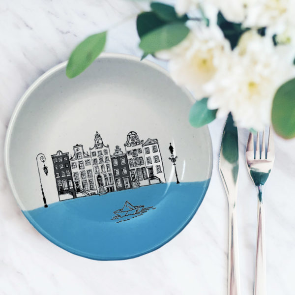 This ceramic plate is handmade by hedgehogs at Darn Pottery and has a drawing of Amsterdam canal houses and a little paper boat. Blue accent color