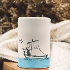 A handmade tumbler with a drawing of a hedgehog on a sailboat, probably plotting a daring exploit. Blue accent color.