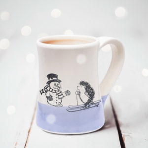 Handmade coffee mug with a drawing of a hedgehog on skis greeting a well-dressed snowman. Lavender accent color