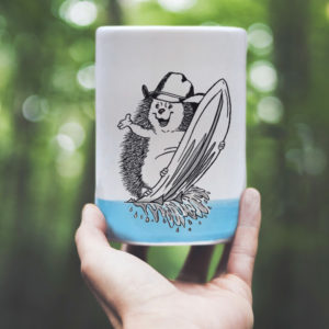 Blue Darn Pottery Tumbler with drawing of a hedgehog surfing and wearing a cowboy hat