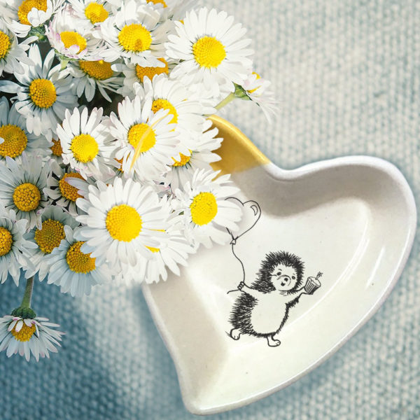 Handmade ceramic heart shaped dish with a drawing of hedgehog heading to a party with a cupcake and a balloon. Gold accent color
