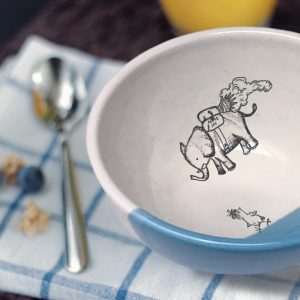 A perfectly sized handmade ceramic bowl for soup with a drawing of an elephant flying over a startled chicken. Blue accent color